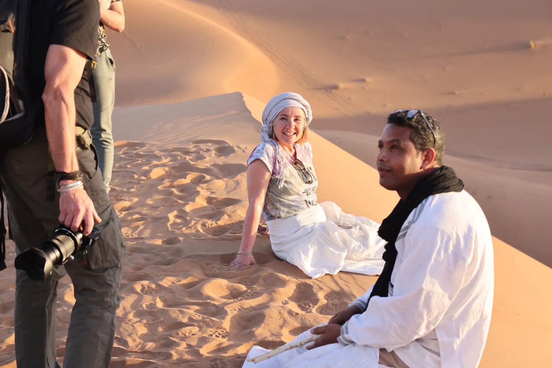 Voyageurs et guide partageant un moment complice au sommet d'une dune de M'Hamid, au coucher du soleil