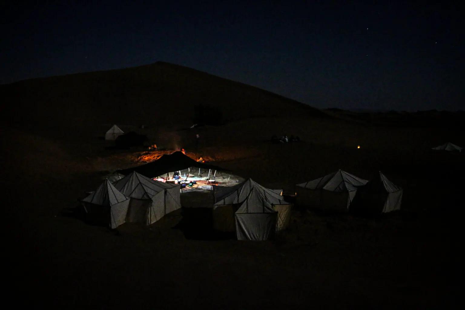Vue nocturne du campement du Bivouac Joudour Sahara, tentes éclairées au pied des dunes